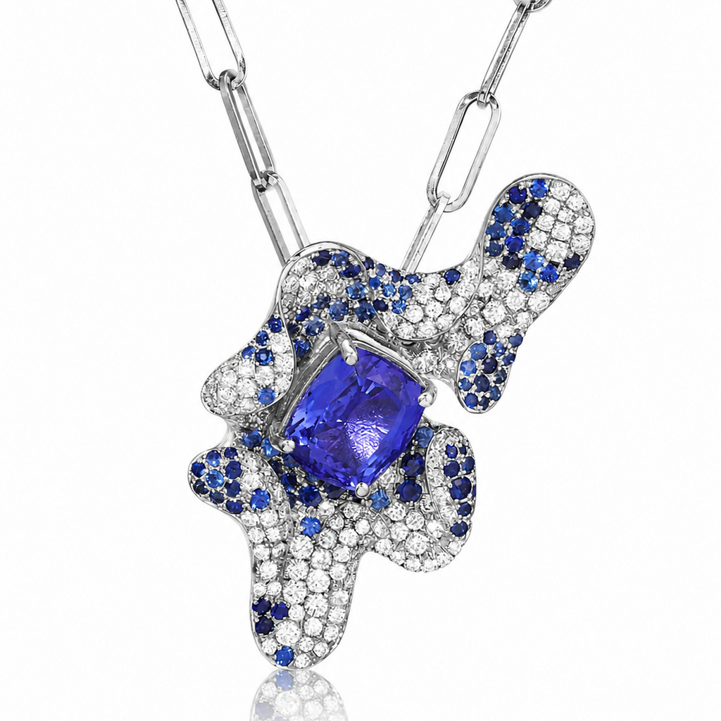 An abstract pendant necklace featuring a large central blue tanzanite gemstone surrounded by pavé-set blue sapphires and clear stones on a silver-toned chain, shown against a white background.
