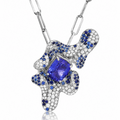 An abstract pendant necklace featuring a large central blue tanzanite gemstone surrounded by pavé-set blue sapphires and clear stones on a silver-toned chain, shown against a white background.