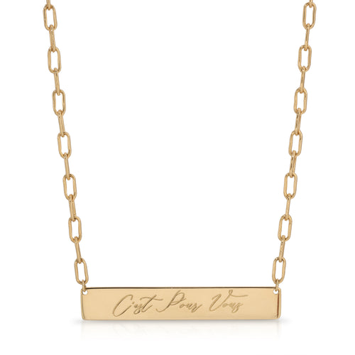 A gold bar necklace with a rectangular pendant engraved with the French phrase 'C'est Pour Vous', suspended from a gold paperclip chain on a white background.