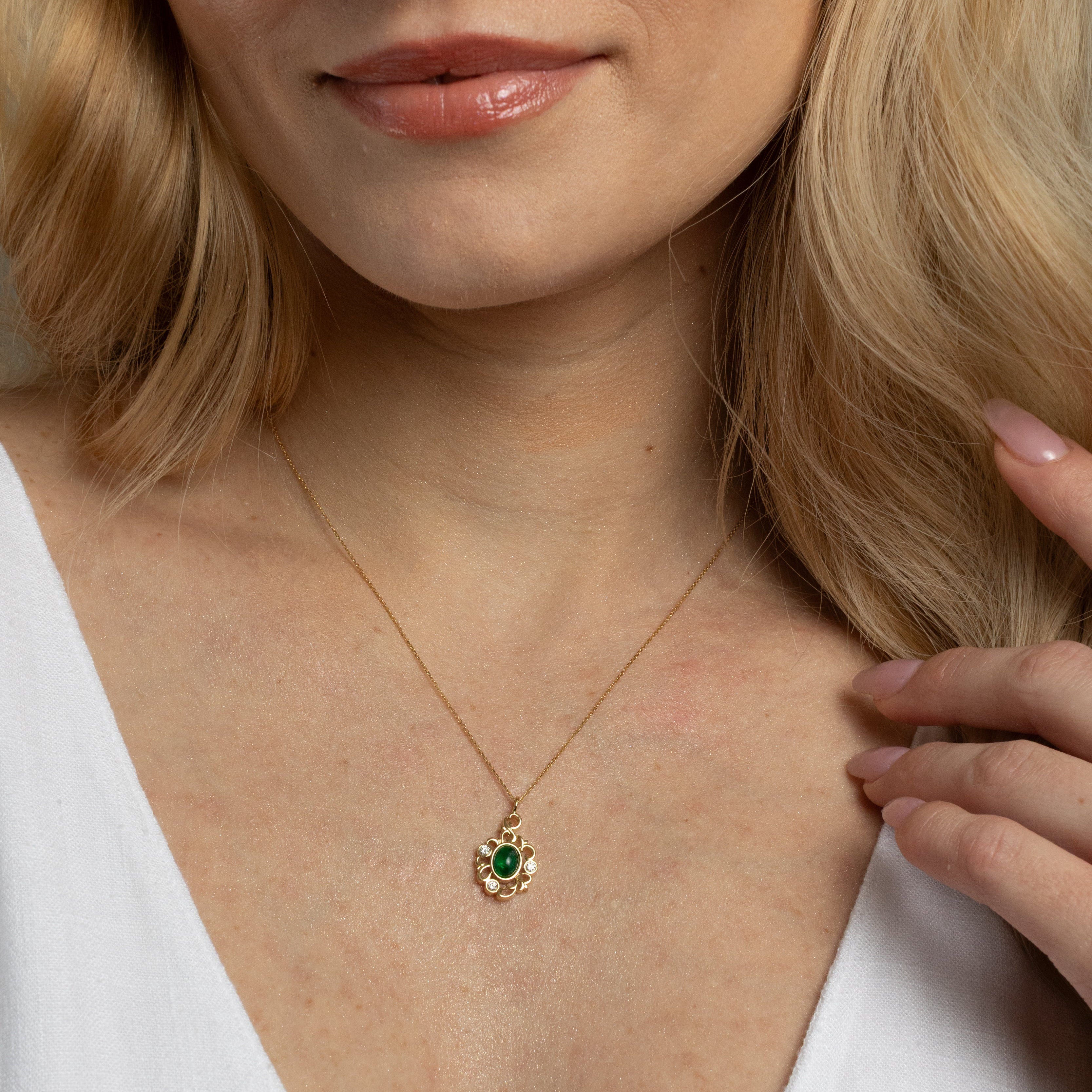 A close-up lifestyle shot of a woman wearing a delicate gold necklace with a small floral pendant featuring a green center stone.