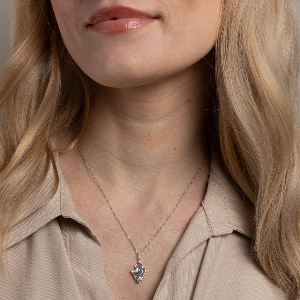 A close-up of a woman wearing a delicate silver pendant necklace with a small, detailed silver charm, paired with a beige collared shirt.