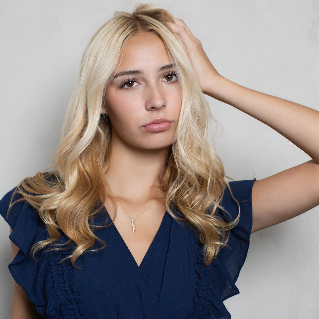 A blonde woman posing in a navy blue ruffled V-neck dress against a light gray textured wall.