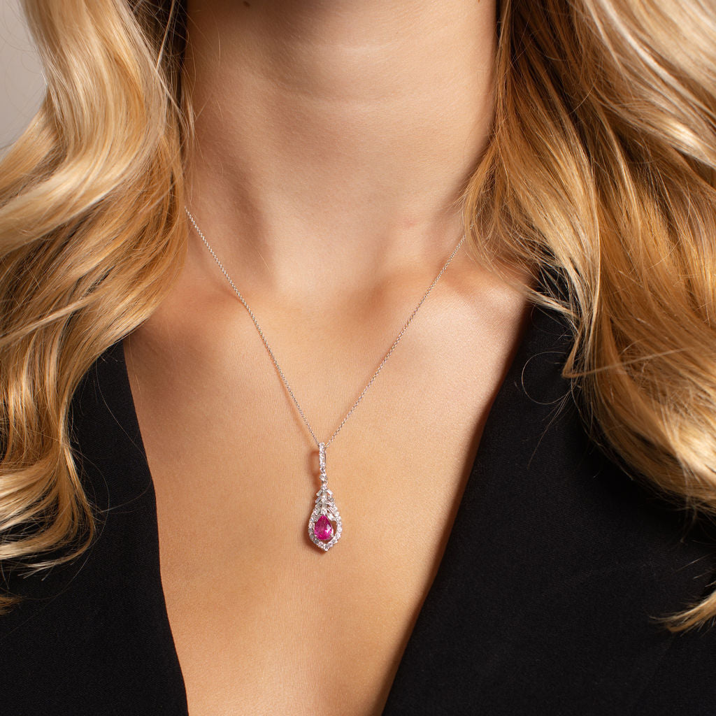 A close-up of a model wearing a silver teardrop pendant necklace with a pink gemstone, styled with a black blazer.