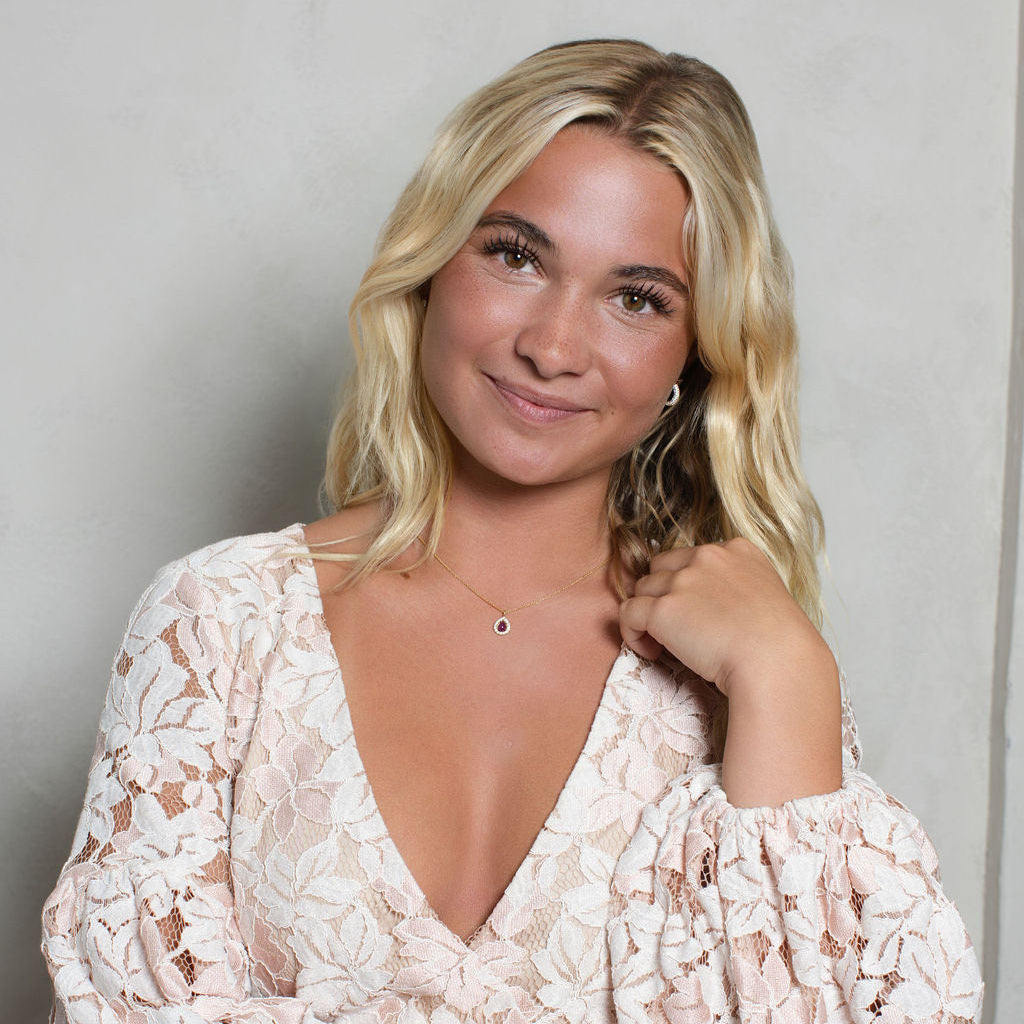 A blonde woman wearing a light pink and white floral lace long-sleeve wrap dress, posing against a neutral light gray wall.