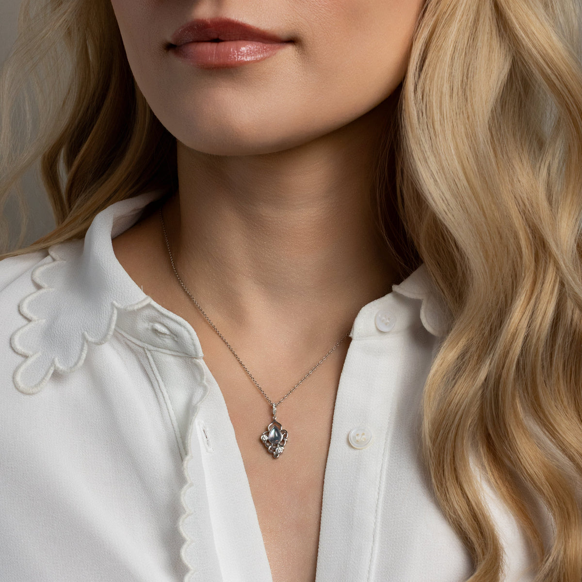 Woman wearing a white blouse and a necklace with a heart pendant.