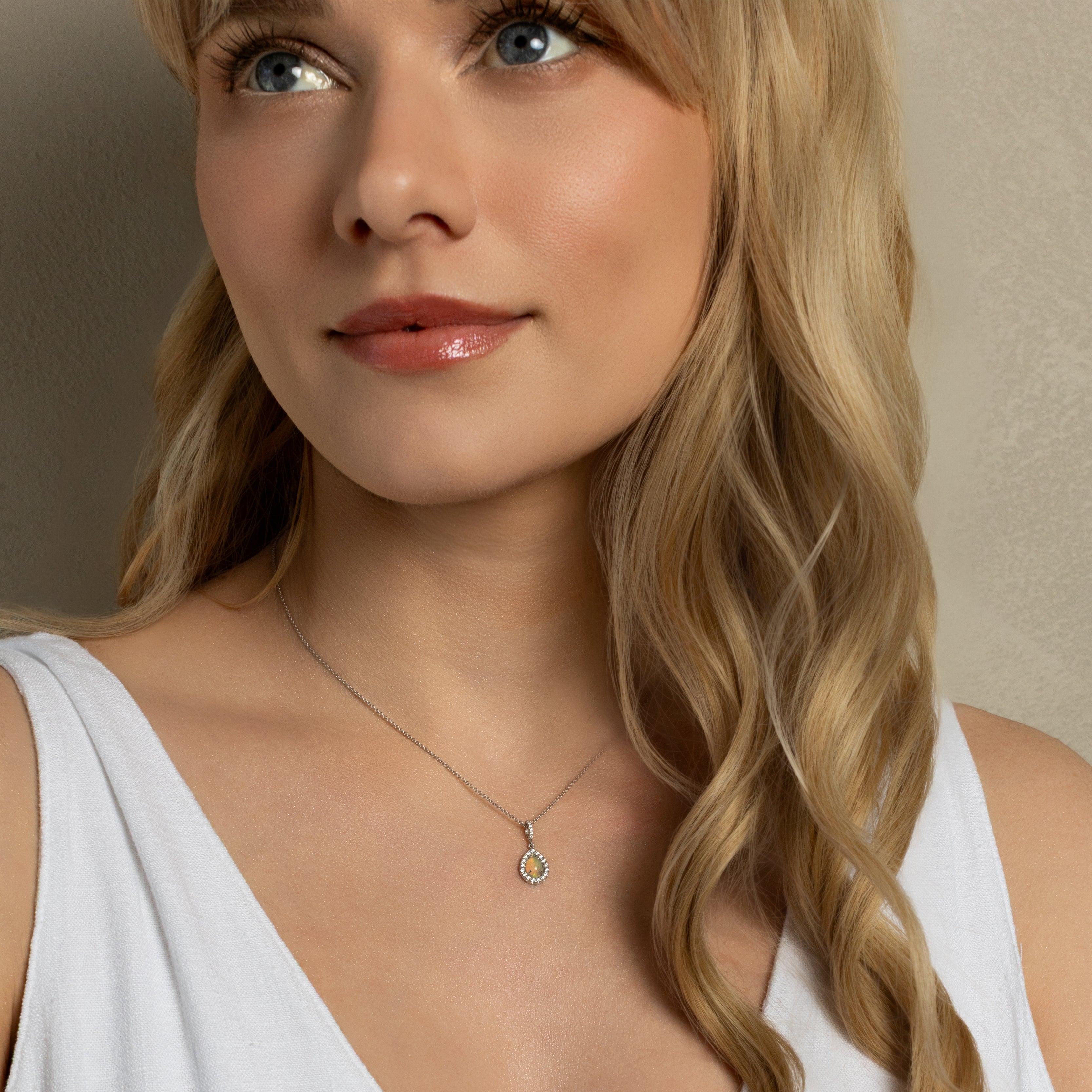 A close-up of a blonde woman wearing a delicate gold necklace with a small circular pendant, paired with a white sleeveless top.