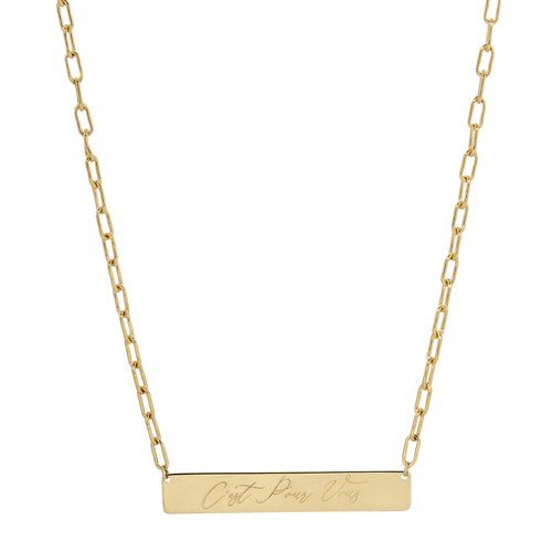 A gold bar necklace with a rectangular pendant engraved with the words 'Just Like That' in cursive script, suspended from a paperclip chain on a white background.