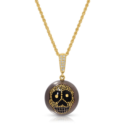 A gold chain necklace with a round pendant featuring a black and gold sugar skull design on a smoky brown background, set against a plain white background.