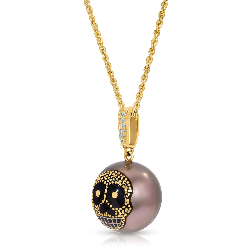 A gold chain necklace with a round pendant featuring a black and gold sugar skull design over a dusty purple-gray pearl, shown on a white background.