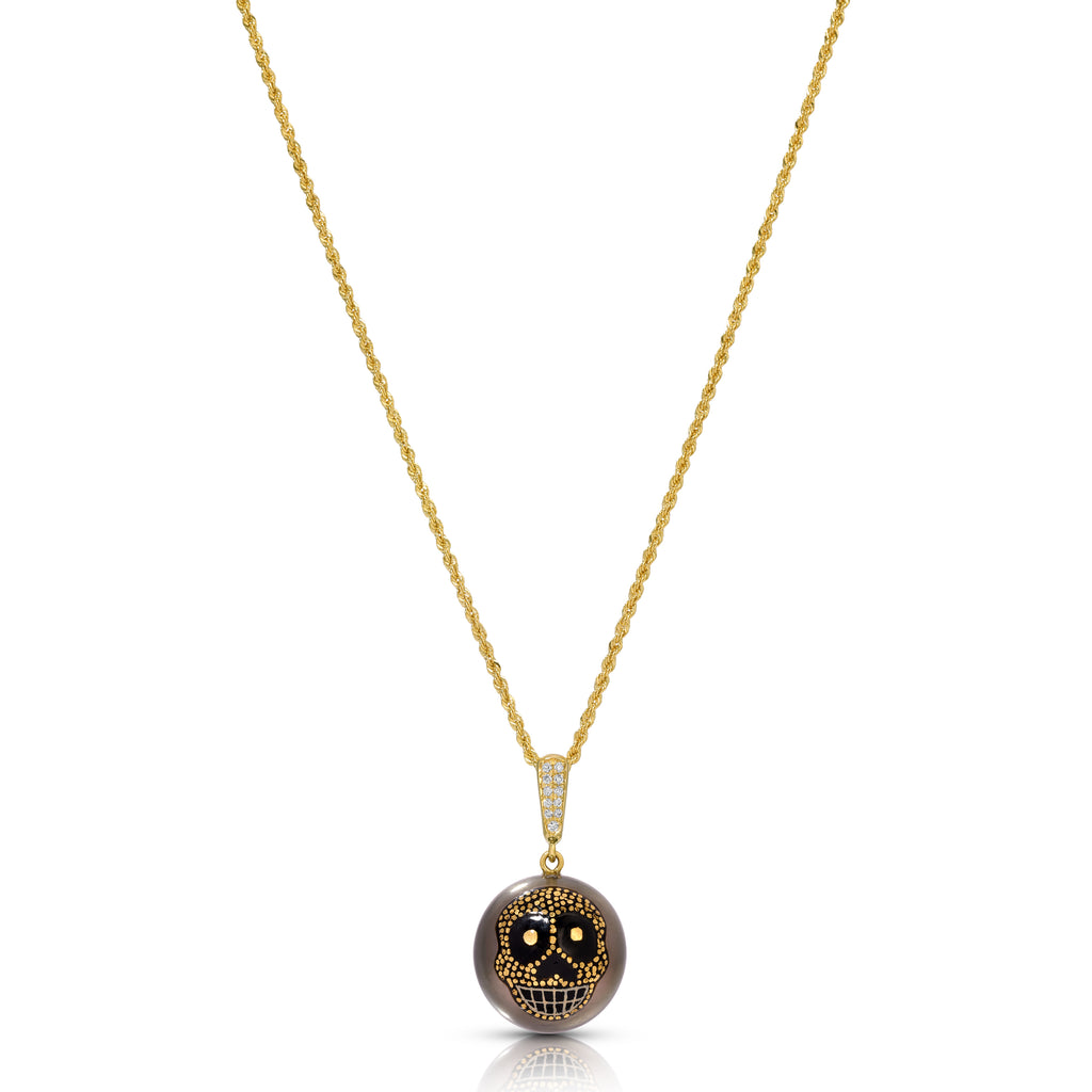 A gold chain necklace with a round pendant featuring a detailed skull design in black and gold, set against a plain white background.