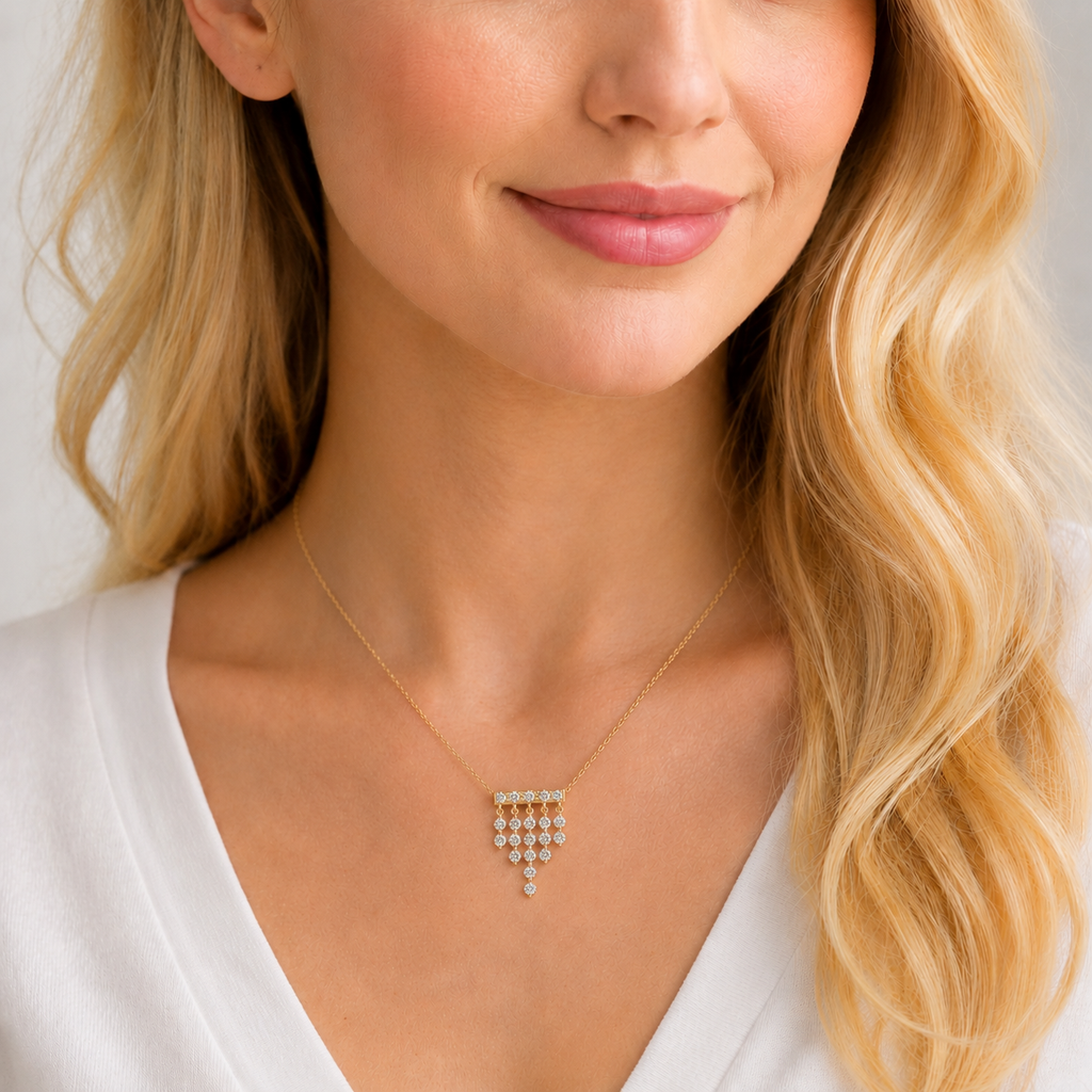 A close-up of a woman wearing a delicate gold necklace with a small geometric cluster pendant set with clear stones, paired with a white top.